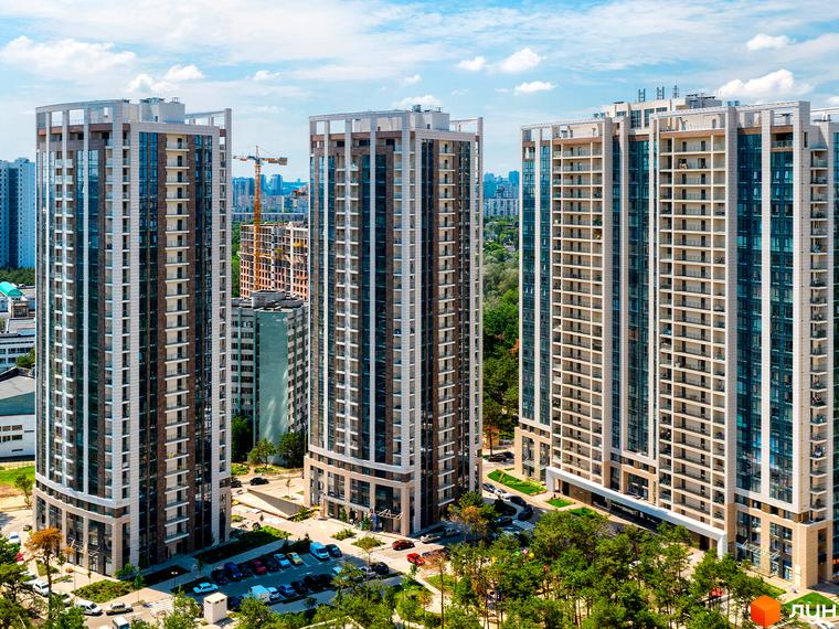 Житловий комплекс Автограф - висотні будинки з панорамними вікнами та балконами. Навколо зелені насадження та облаштована прибудинкова територія з парковкою.