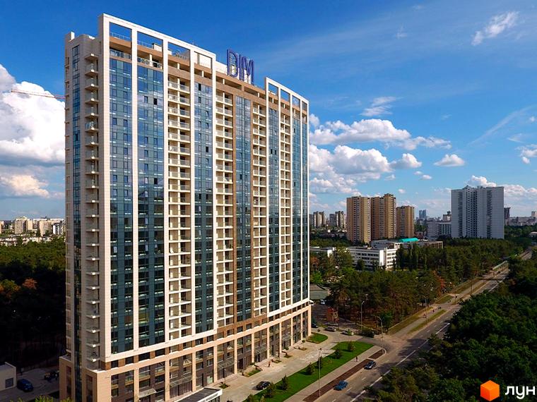 Житловий комплекс Автограф – висотна новобудова зі скляним фасадом та білими вертикальними елементами, оточена зеленню та дорогою.