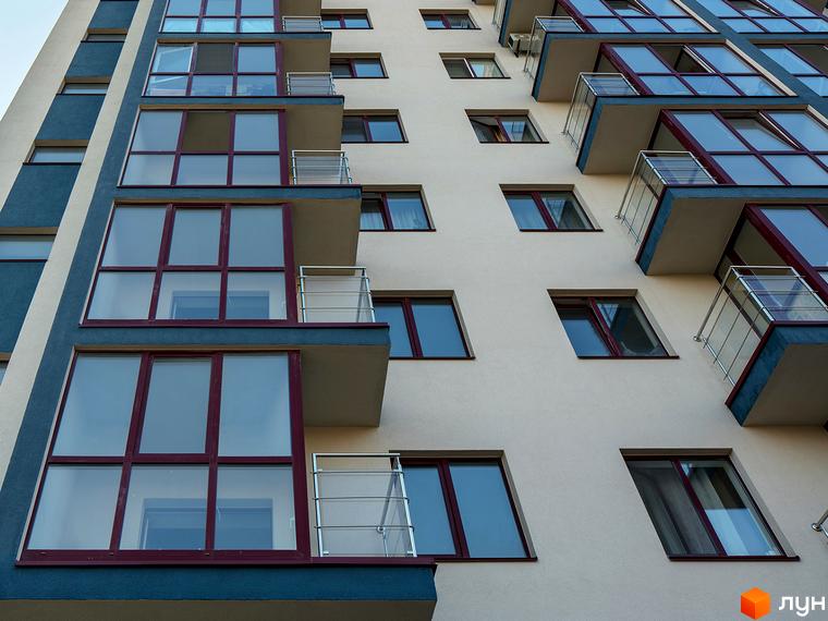 Фамільний житловий комплекс: фасад будівлі з великими вікнами та балконами. Зовнішній вигляд новобудови з панорамним склінням.