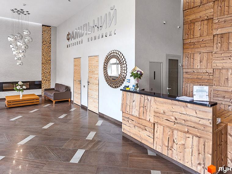 Житловий комплекс Фамільний: просторий хол з дизайнерським освітленням, дерев'яною обшивкою стін та стійкою рецепції. Сучасний дизайн інтер'єру.