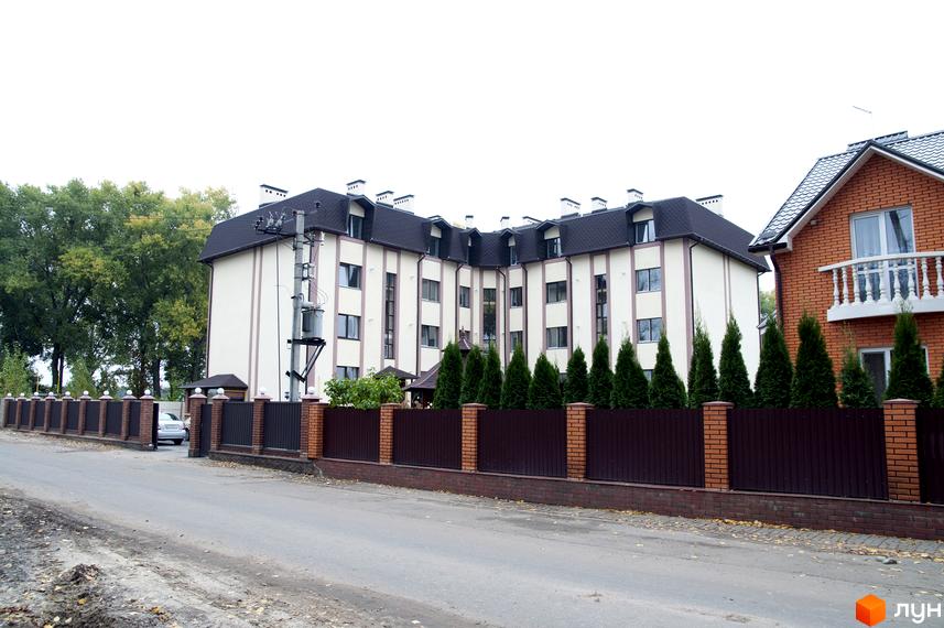 Зовнішній вигляд житлового комплексу на вул. Червоноармійська, 14. Огороджена територія з парканом та зеленими насадженнями.