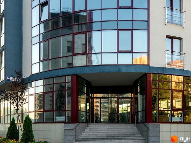 Житловий комплекс Фамільний: фасади будівель з великою кількістю скління та виходом до входу. Прибудинкова територія з деревами та квітами.