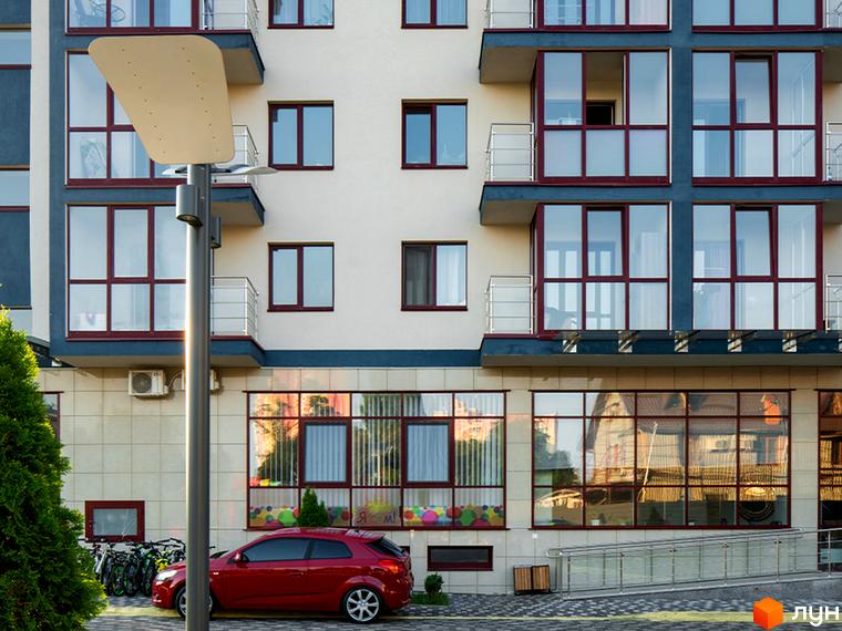 Фамільний житловий комплекс: фасади будівель з великими вікнами та балконами, червоний автомобіль та велосипеди біля будинку.