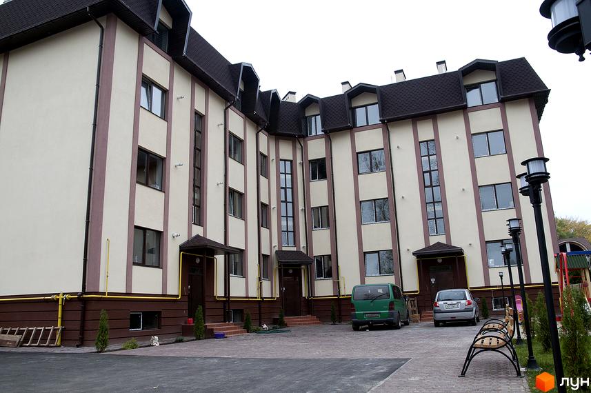 Будинок житлового комплексу на вул. Червоноармійська, 14, з світлим фасадом та коричневими вертикальними смугами. Прибудинкова територія з парковкою та лавками.