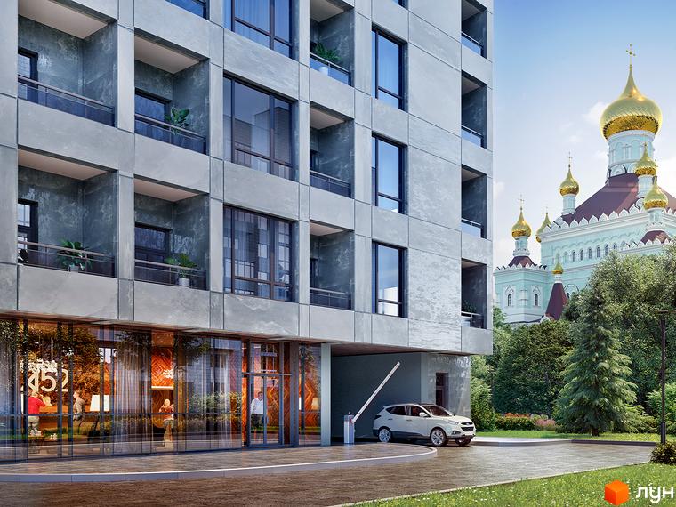 Житловий комплекс А52 з сірим фасадом, великими вікнами та балконами. Поруч зелені насадження, парковка та церква із золотими куполами.
