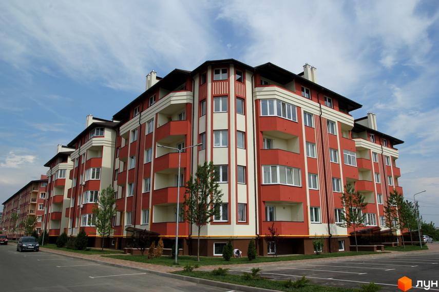 Житловий комплекс Щасливий з яскравими фасадами та балконами. Прибудинкова територія озеленена деревами та газонами.