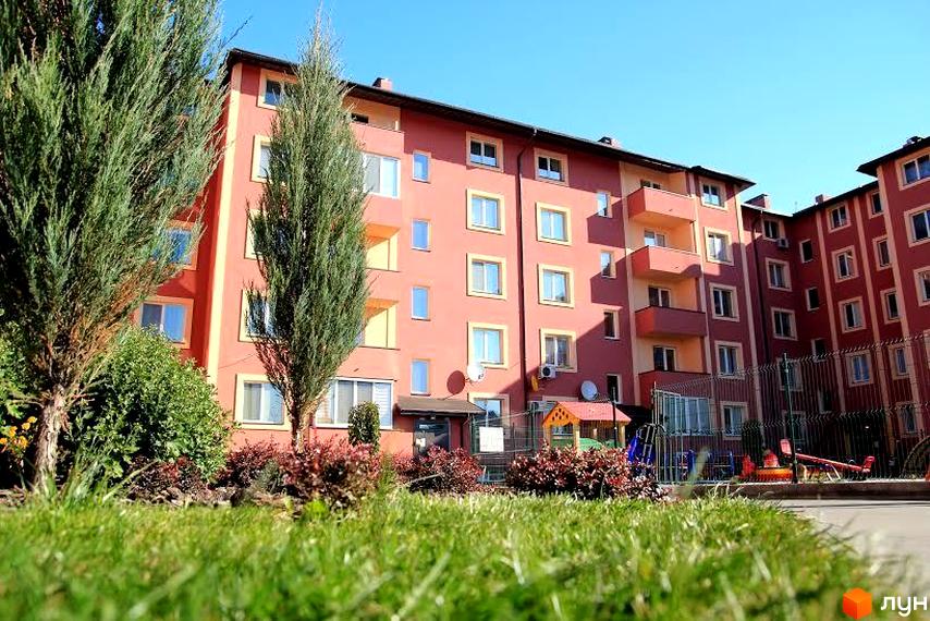 Житловий комплекс Щасливий з яскравими фасадами та прибудинковою територією, озелененою газонами і дитячим майданчиком.