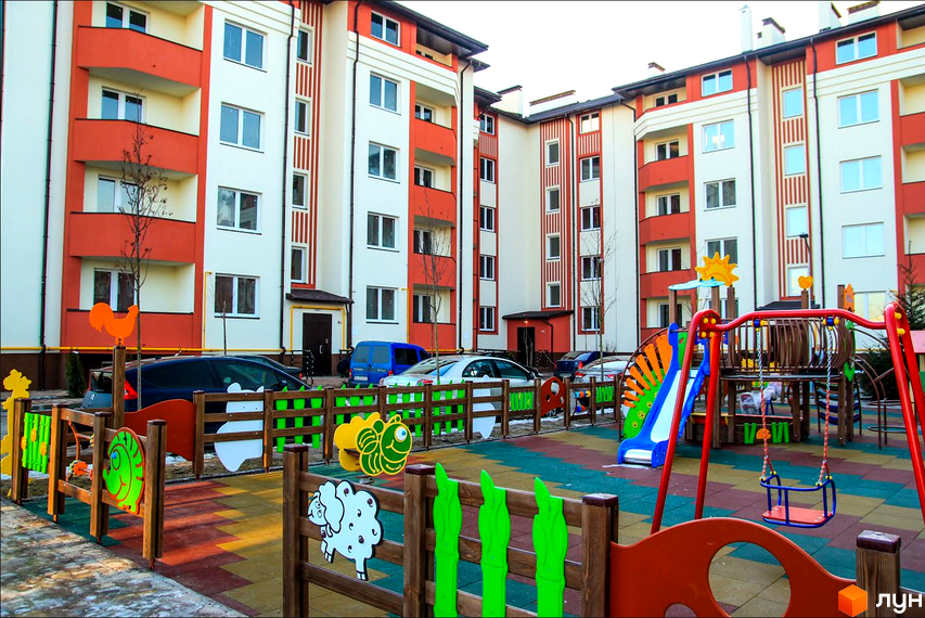 Житловий комплекс Щасливий з червоно-білим фасадом та прибудинковою територією з дитячим майданчиком.