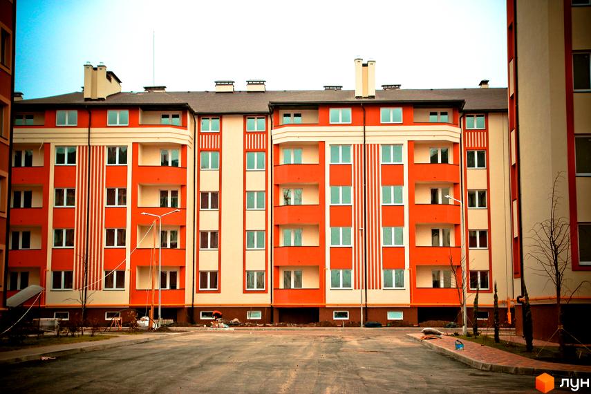 Житловий комплекс Щасливий: фасади будівель у помаранчево-бежевих тонах з вертикальними смугами. Прибудинкова територія з дорогою та тротуаром.