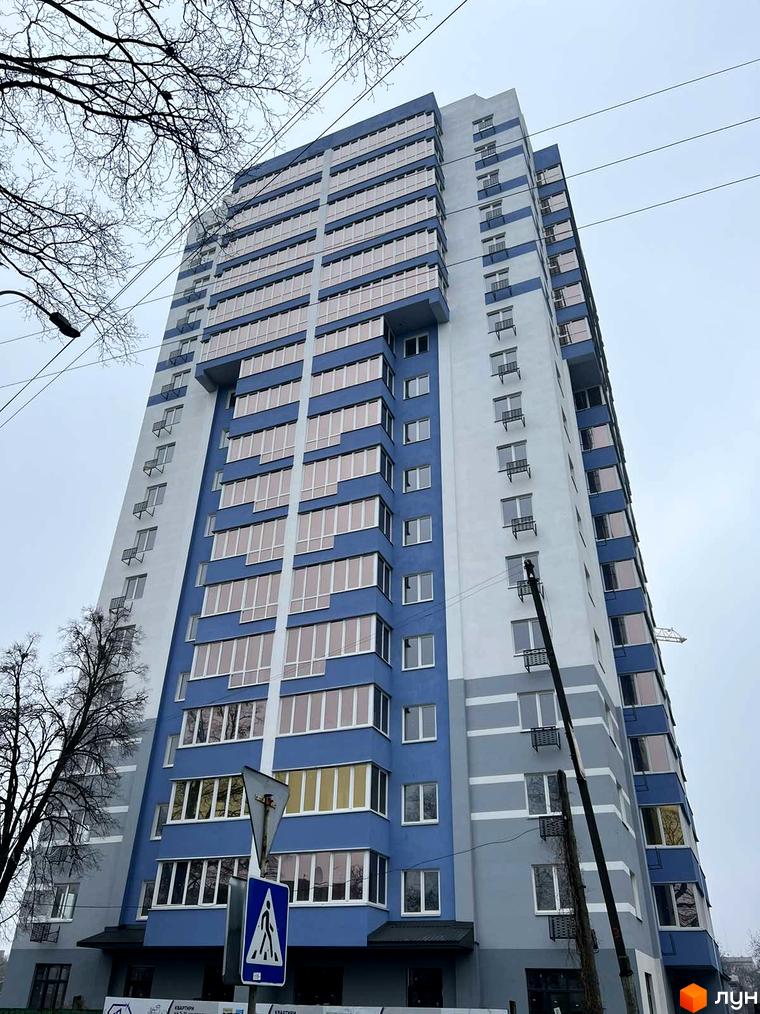 Зовнішній вигляд новобудови ЖК Diamond Hall з синіми та сірими фасадами, великою кількістю вікон та балконів. Навколо будівлі видно дерева та елементи міської інфраструктури.