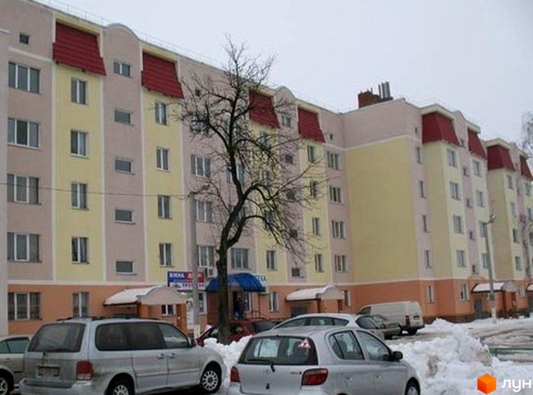 Житловий комплекс на вул. Жовтнева, 55, з фасадом жовто-рожевого кольору та червоними дахами. Прибудинкова територія з автомобілями та деревами.