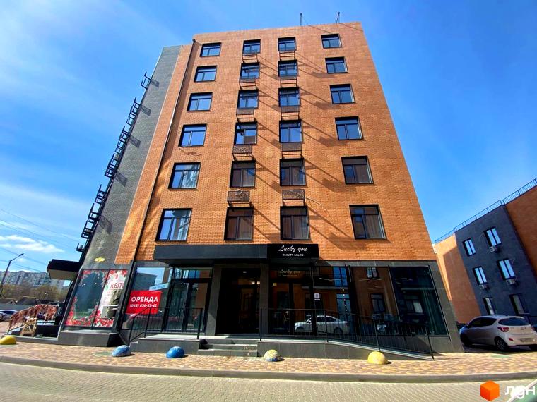Новобудова Plaza Kvartal з цегляним фасадом та великими вікнами. Перед будинком облаштований вхід з пандусом та квітковими клумбами.
