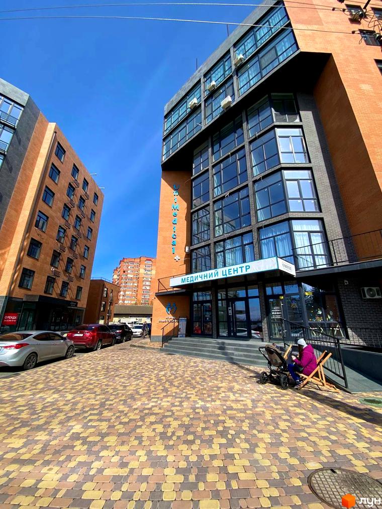 Зовнішній вигляд будівлі житлового комплексу Plaza Kvartal з цегляним фасадом та великими вікнами. Прибудинкова територія вимощена бруківкою.