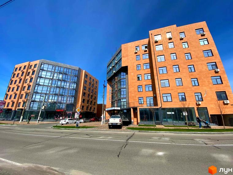 Новобудова Plaza Kvartal з цегляним фасадом та великими вікнами, розташована біля дороги з автомобілями та зеленою зоною.