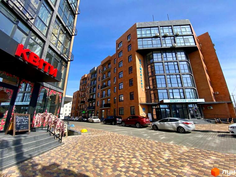 Новобудова ЖК Plaza Kvartal з цегляним фасадом та великими вікнами, розташована на бруківці з зеленими насадженнями.