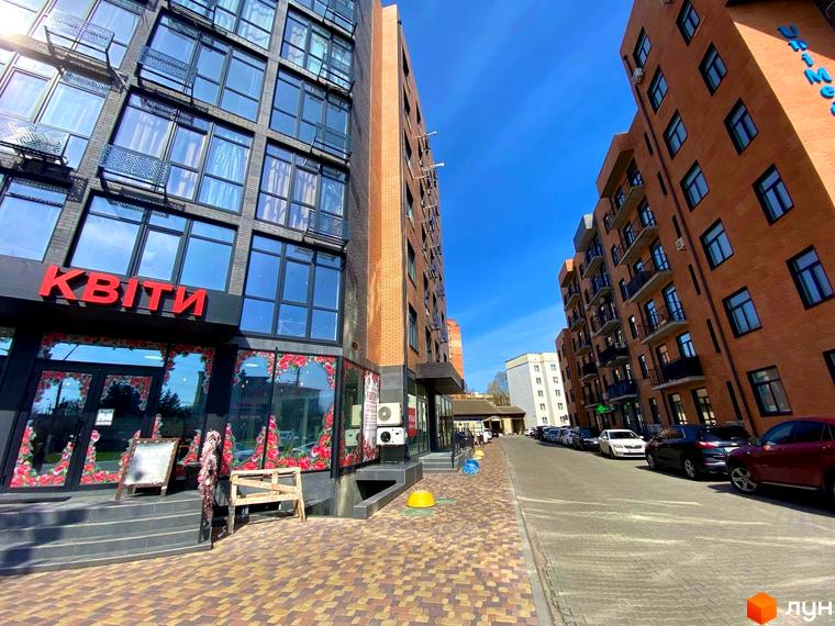 Житловий комплекс Plaza Kvartal. Сучасна цегляна новобудова з великими вікнами та балконами, розташована вздовж вулиці з припаркованими автомобілями.