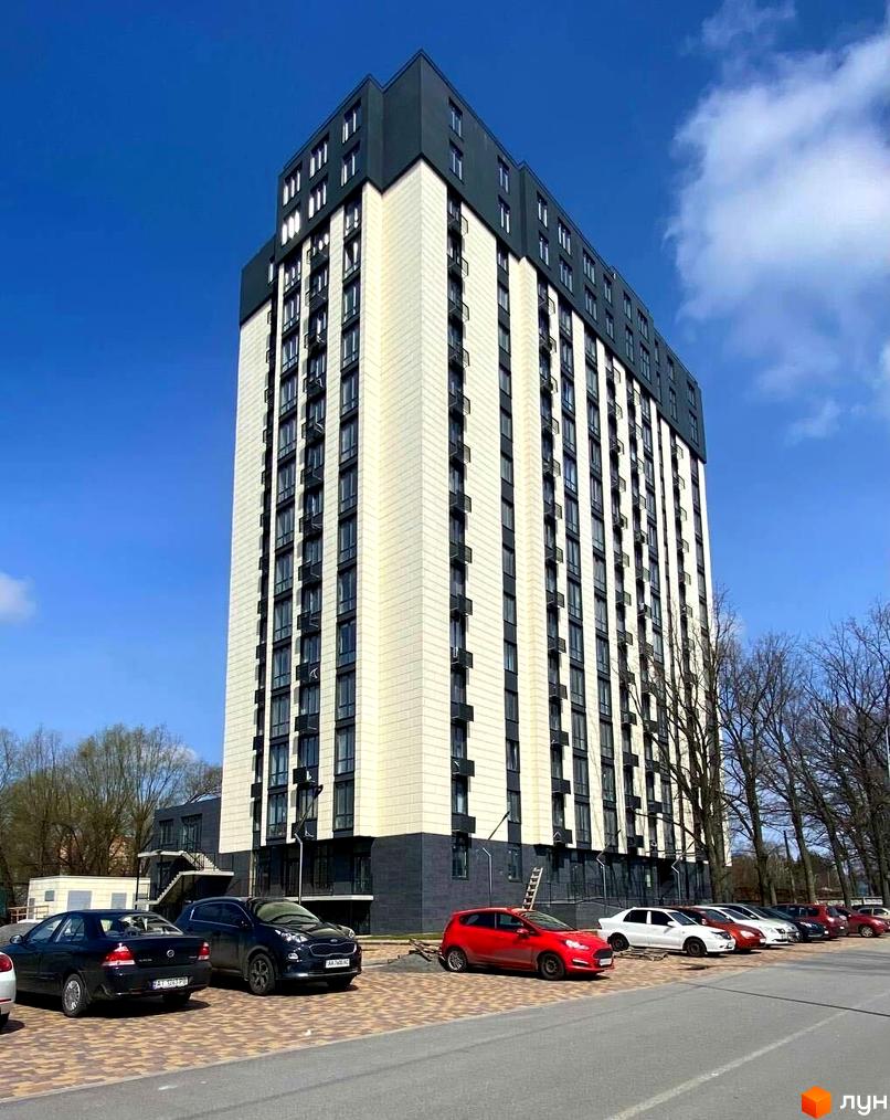 Багатоповерхова новобудова Park Plaza з світлим фасадом та темними вікнами. Поруч розташована парковка з автомобілями та дерева.