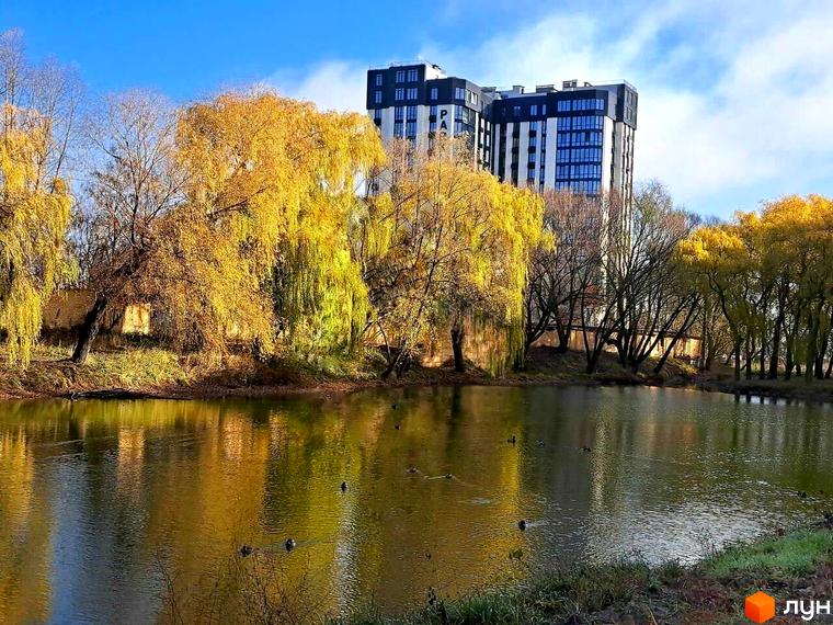 Багатоповерховий Житловий комплекс Park Plaza з темним та світлим фасадом біля осіннього озера з жовтими деревами та качками.