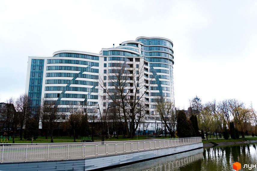 Зображення Житлового комплексу Parus з великими вікнами та заокругленими формами. Вид на будівлю з боку річки та пішохідної зони.