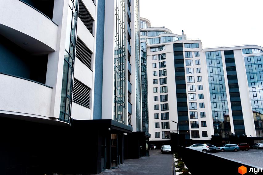 Зовнішній вигляд Новобудови Parus. Багатоповерховий будинок з великими вікнами та прибудинковою територією з парковкою.