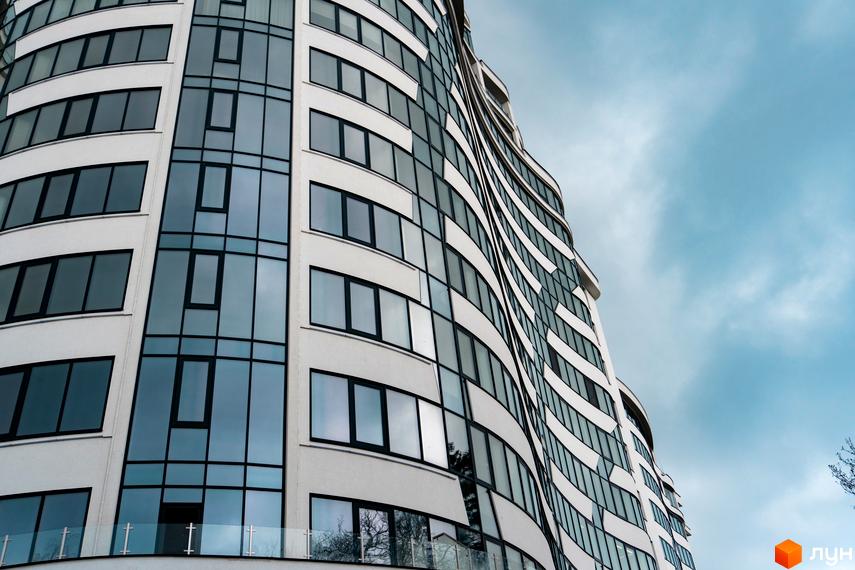 Зображення фасаду Житлового комплексу Parus з великими вікнами. Багатоповерхова будівля на фоні хмарного неба.