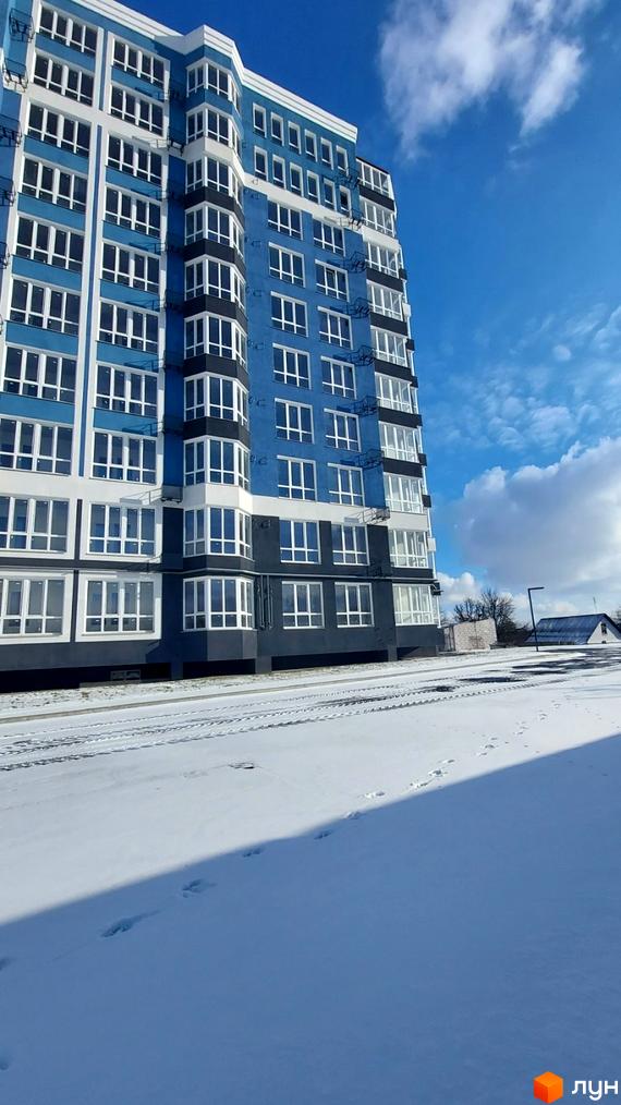 Зовнішній вигляд житлового комплексу Лісовий: багатоповерхова синьо-біла будівля з численними вікнами на тлі блакитного неба та засніженої території.