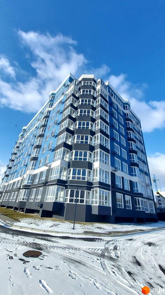 Новобудова Лісовий: багатоповерховий будинок синього та темно-сірого кольорів з великими вікнами. Навколо сніжна прибудинкова територія.