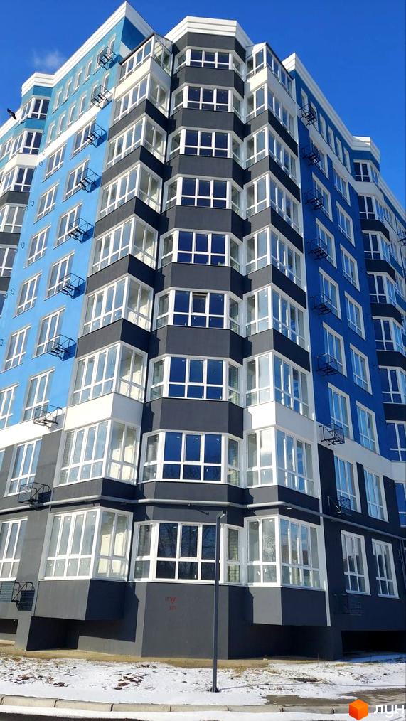 Зовнішній вигляд новобудови ЖК Лісовий з блакитним та сірим фасадом, великою кількістю вікон та балконів. Навколо будинку видно сніг та дорогу.