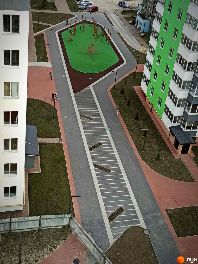 Вид на житловий комплекс з висоти пташиного польоту. На фото видно зелену територію з дитячим майданчиком та будівлі з білими та зеленими фасадами.