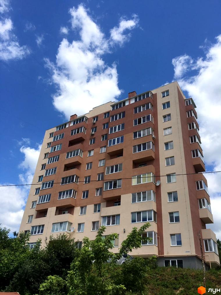 Багатоповерховий житловий комплекс на вулиці Джона Леннона, 1, 3, з коричнево-бежевим фасадом та численними вікнами, оточений зеленню.