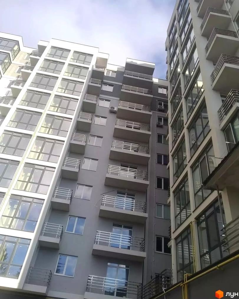 Житловий комплекс Фортеця з балконами та панорамними вікнами. Сірий фасад будівлі з великою кількістю поверхів, видно блакитне небо.