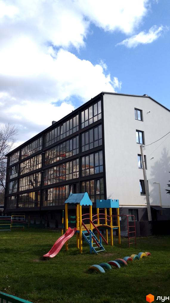 Житловий комплекс Happy House: білий будинок з великими вікнами та зелений двір з дитячим майданчиком.