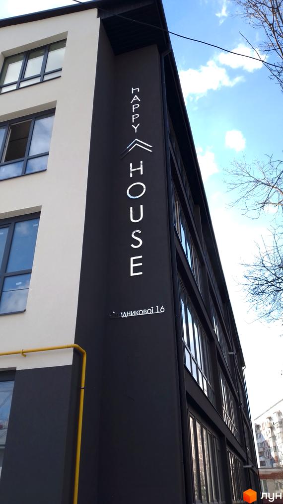 Фасад Житлового комплексу Happy House виконаний у темних та світлих відтінках, з великими вікнами. На будинку видно вивіску та жовту газову трубу.