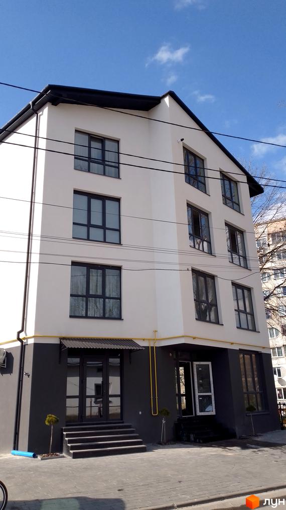 Фасад житлового комплексу Happy House з великими вікнами та сірою цокольною частиною. Поруч розташовані сходи та вхідні групи.