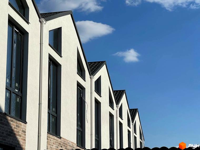 Таунхауси West Homes з білою штукатуркою та темними вікнами на тлі блакитного неба з хмарами. Зовнішній вигляд будинків з акуратними дахами та цегляною основою.