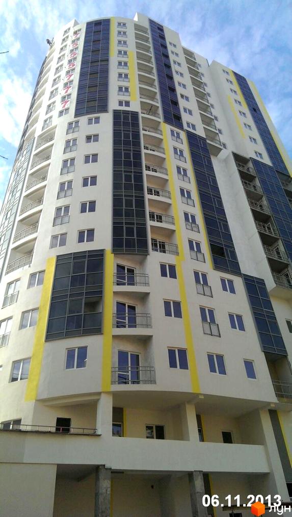 Житловий комплекс Аксіома - висотна новобудова з панорамним склінням та балконами. Зовнішній вигляд фасаду з білими стінами та жовтими акцентами.