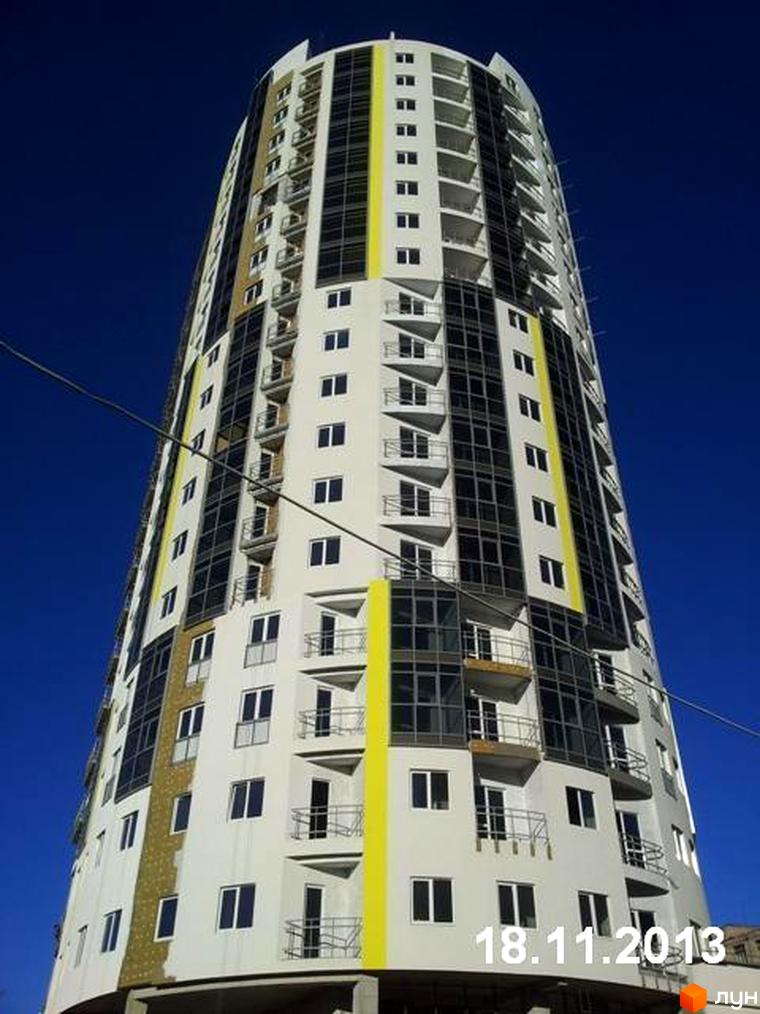 Житловий комплекс Аксіома - висотна новобудова з біло-жовтим фасадом та панорамними вікнами. Будинок має багато балконів та сучасний дизайн.