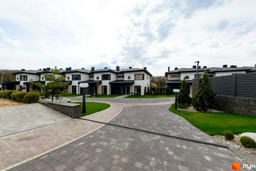 Зовнішній вигляд котеджного містечка КМ SHERWOOD: білі двоповерхові будинки з чорними дахами та вікнами. Прибудинкова територія з доглянутими газонами, доріжками з бруківки та декоративними деревами.