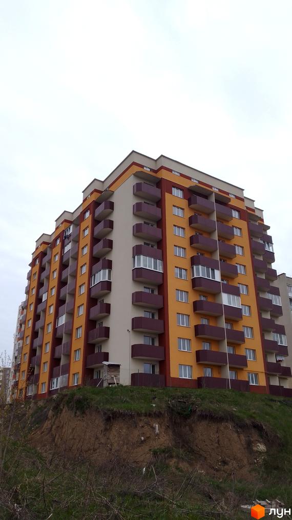 Багатоповерховий житловий комплекс на вулиці Смакули, 2, з яскравим фасадом у жовто-бордових тонах та численними балконами. Навколо будинку розташована зелена ділянка з деревами та схилом.