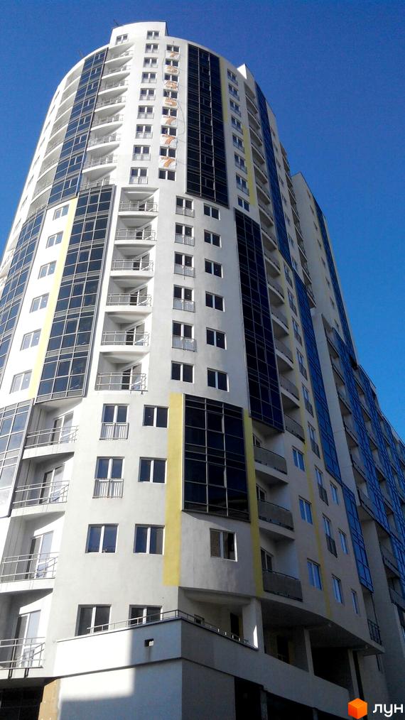 Житловий комплекс Аксіома - висотна новобудова з панорамним склінням та балконами. Зовнішній вигляд будівлі з білими та сірими фасадами, жовтими акцентами та темними вікнами.