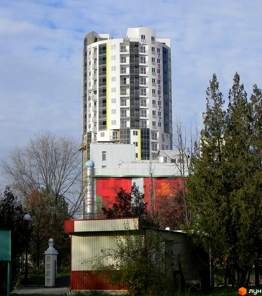 Житловий комплекс Аксіома - висотна будівля з балконами та панорамними вікнами, оточена деревами та іншими спорудами.