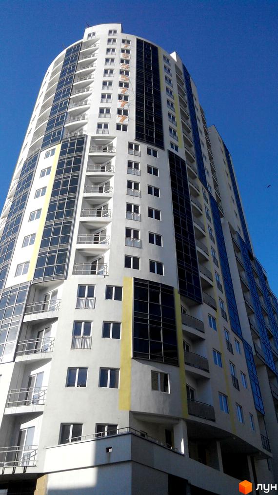 Житловий комплекс Аксіома - висотна будівля з панорамними вікнами та балконами. Фасад оздоблений білими та темними панелями, з яскравими жовтими акцентами.