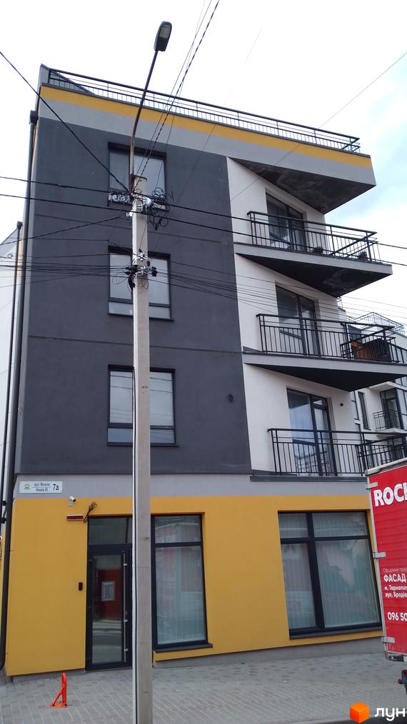 Багатоповерховий будинок з балконами, фасадом жовтого та сірого кольорів. Біля будинку стовп з ліхтарем та дротами.