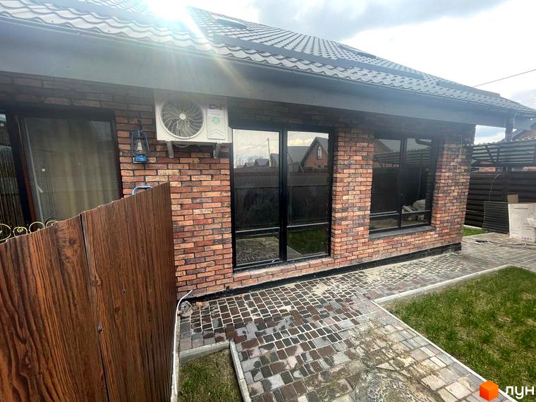 Котеджне містечко КМ Одноповерховий Київ - Віта-Поштова. Зовнішній вигляд будинку з цегляною кладкою та великими вікнами, вимощена доріжка та зелений газон.