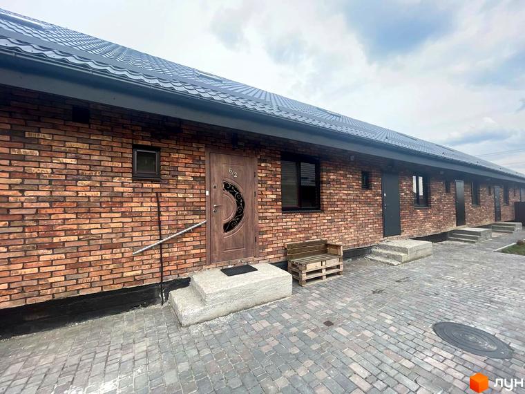 Котеджне містечко КМ Одноповерховий Київ - Віта-Поштова. Фасад будинку з червоної цегли, вхідні двері з візерунком, вимощені бруківкою двір.