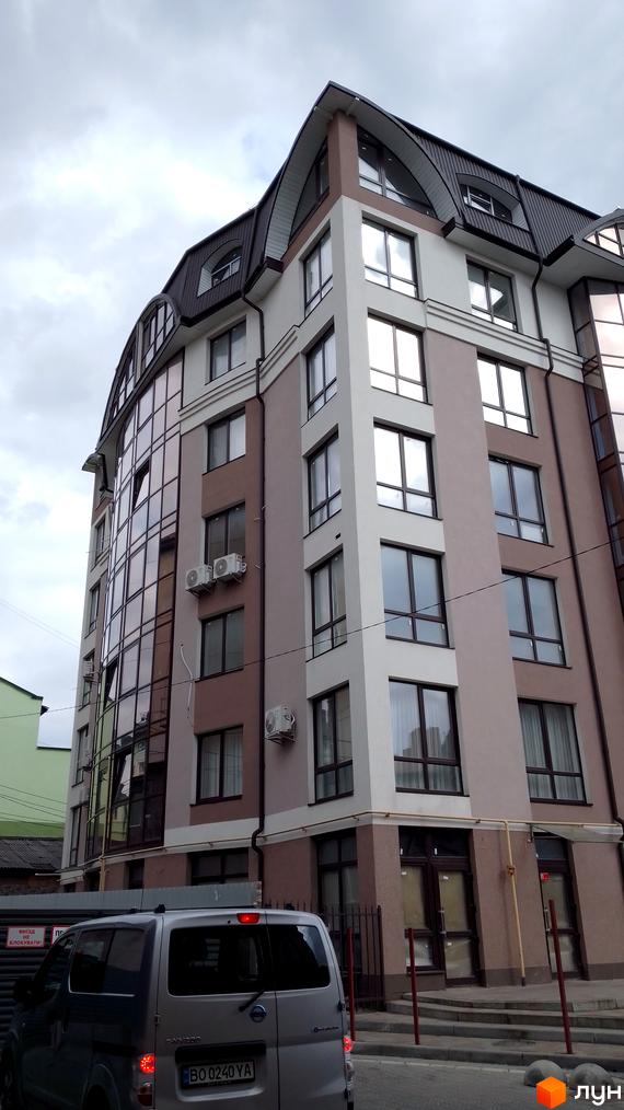 Будівля Житлового комплексу на бул. Шевченка, 31б, має вигнутий дах та комбінований фасад зі скляними елементами. На прилеглій території припаркований автомобіль.