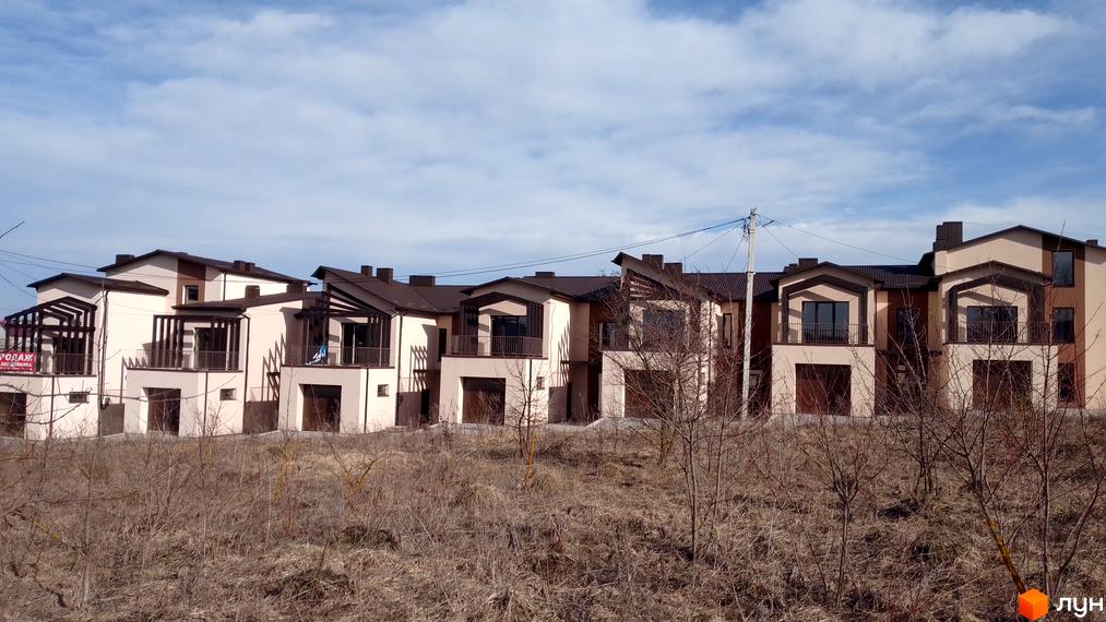 Котеджі по вул. Січових Стрільців: двоповерхові будинки з бежевими фасадами, коричневими дахами, балконами та гаражами. Навколо суха трава.