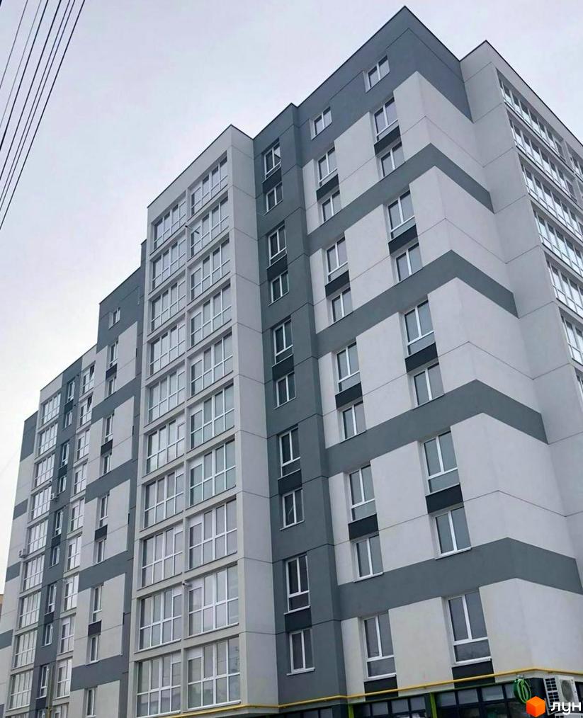 Зовнішній вигляд новобудови на вул. Білогірська з сірими та білими фасадами, великою кількістю вікон. Будинок має багатоповерхову структуру з чіткими геометричними формами.