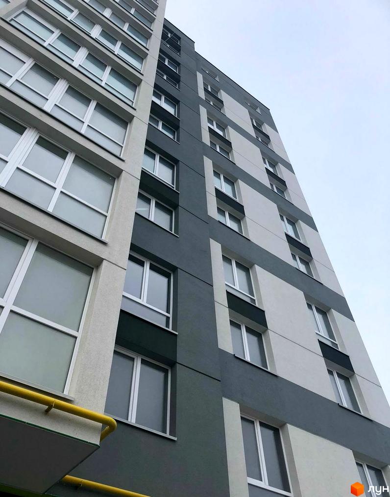 Зовнішній вигляд будинку житлового комплексу на вул. Білогірська, 12. Багатоповерхова новобудова з сірими та білими фасадами та великою кількістю вікон.