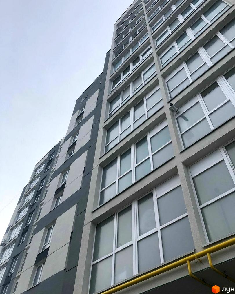 Зовнішній вигляд новобудови на вул. Білогірська з сіро-білим фасадом та численними вікнами. Опис фасаду будівлі.